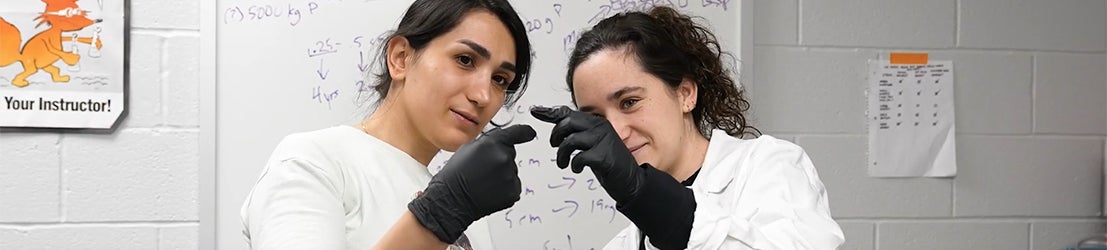 Two BIO students holding and observing a small material in a classroom.
