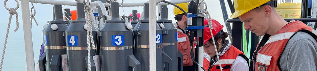 Two EVS students in safety gear conducting research on a boat.
