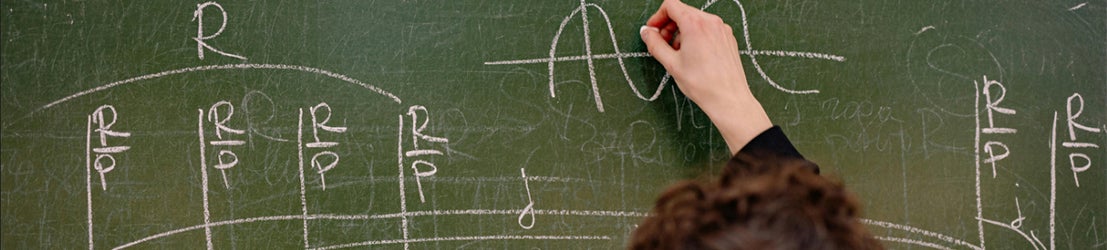 A professor graphing a math equation on a green chalk board.
