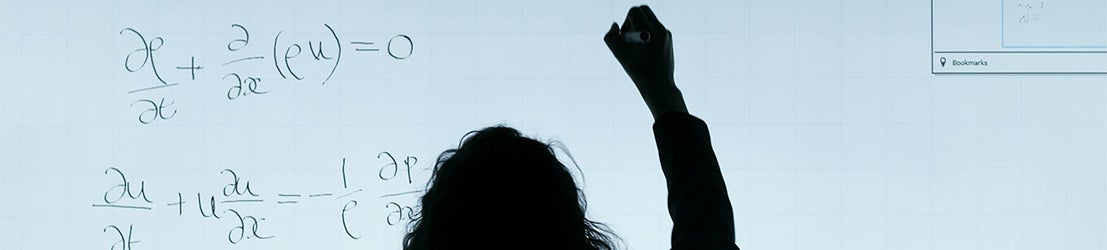 A female professor writing math equations on smart whiteboard in a classroom.