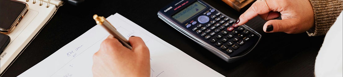 A female student sitting down with a desk solving math equations with a black calculator.