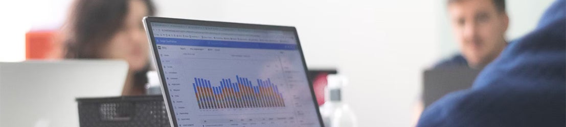 A student in a blue sweater working on graphs on a laptop along with two other students in a classroom.