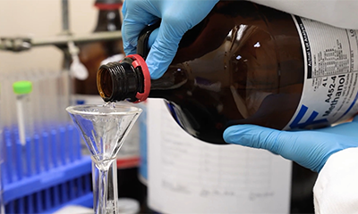 A student pouring chemical liquid into a flask in a lab.