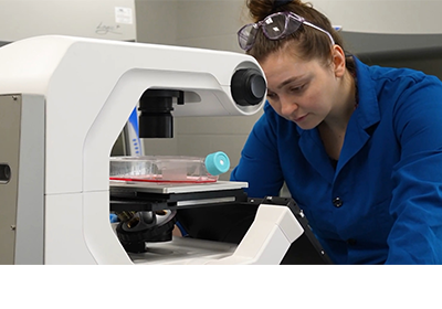 A student in a blue lab coat working on research in a classroom.