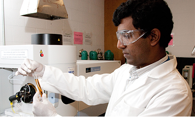 A student in a white lab coat handling research equipment in a classroom.
