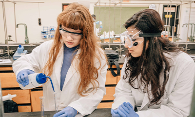 Two students handling research equipment in a lab.
