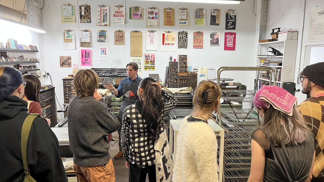 Students on a field trip visiting a printmaking studio listening to an art professional