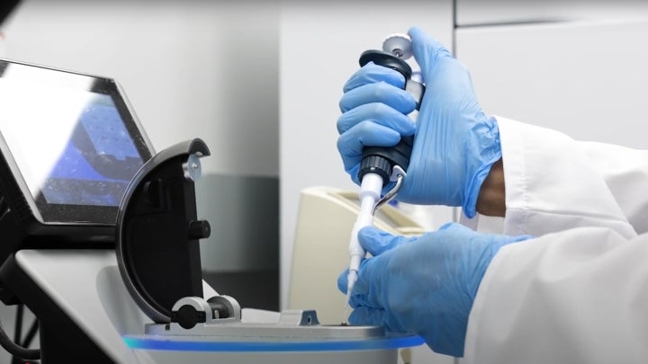 A BIO student in a lab coat with blue gloves handling research equipment.
