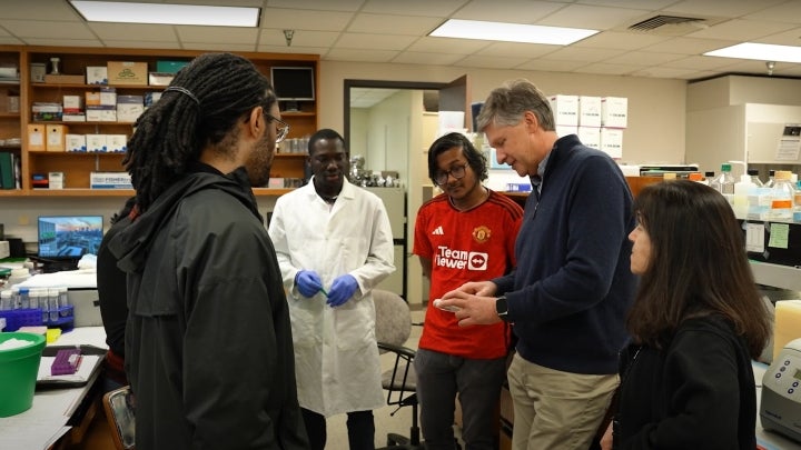 A group of BIO students and professors discussing in a busy classroom laboratory.