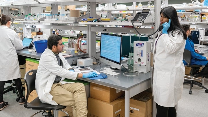 Multiple BIO students in lab coats conducting experiments in a laboratory facility.