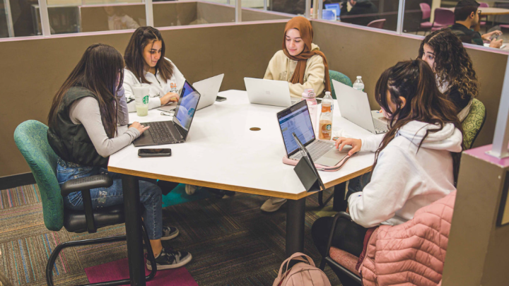 A group of five female students studying with laptops around a table at the CSU library.