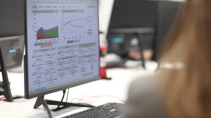 A female student working on data analytics and graphing on a computer monitor in a classroom.