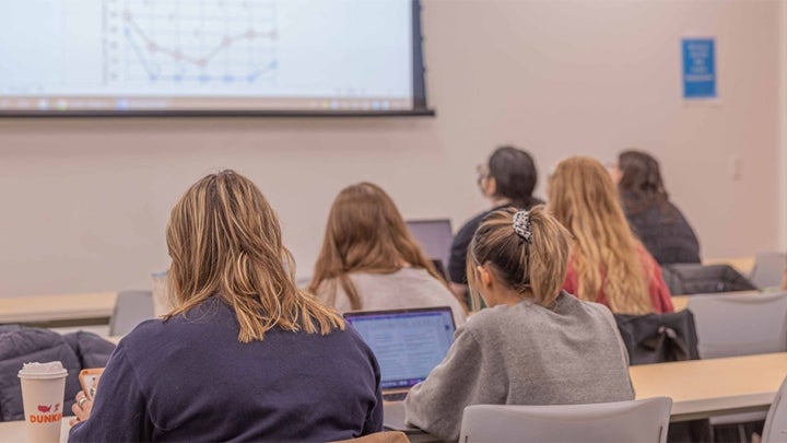Multiple students sitting in a classroom looking forwards towards a whiteboard with a math graph in a classroom.