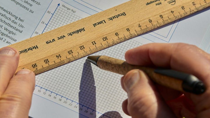 A student drawing a graph on a textbook with a ruler.