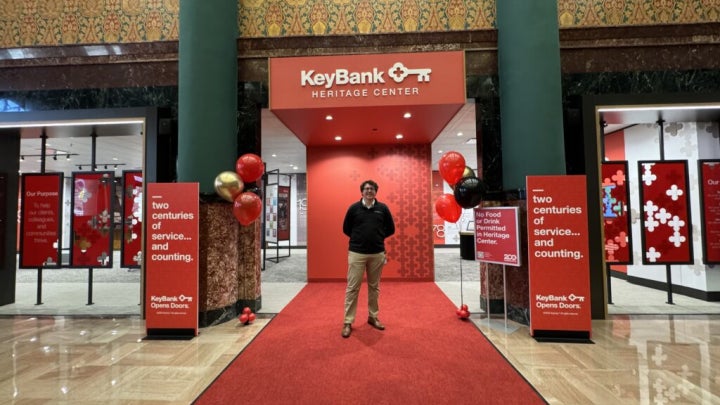Andrew Zelina standing on a red carpet in front of the KeyBank Heritage Center entrance, surrounded by red and black balloons and display signs.