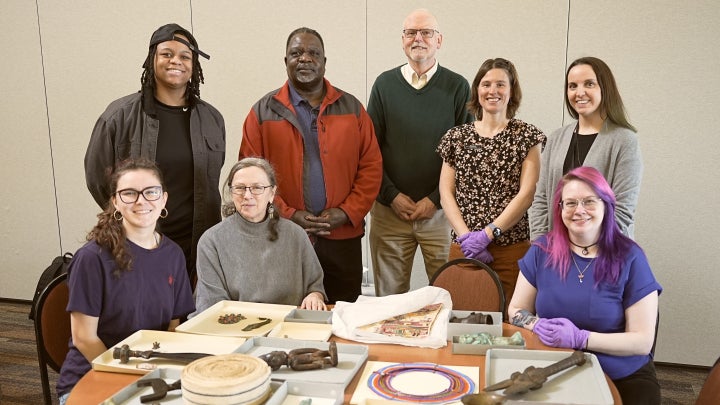 Group of people standing and seated around a table displaying historical artifacts.