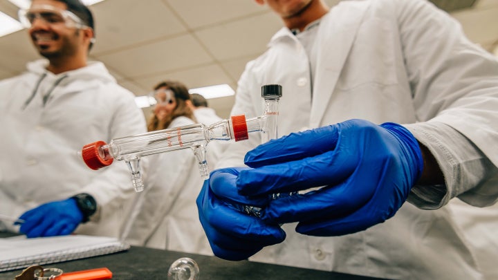 A group of students in white lab coats handling research equipment in a lab.