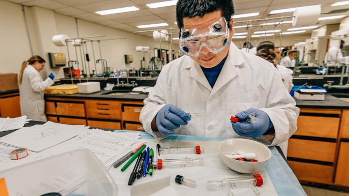 A student in a white lab coat working on research in a lab.