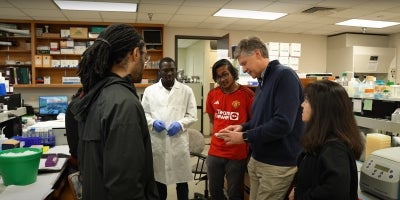 A group of BIO students and professors discussing in a busy classroom laboratory.