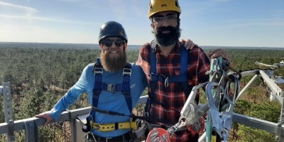 A male professor and a male student wearing EVS PPE conducting research while posing for picture on top of a lookout tower.