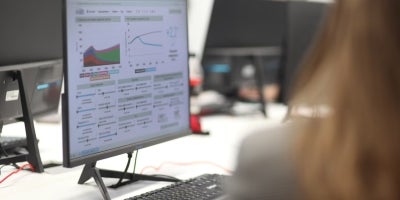 A female student working on data analytics and graphing on a computer monitor in a classroom.