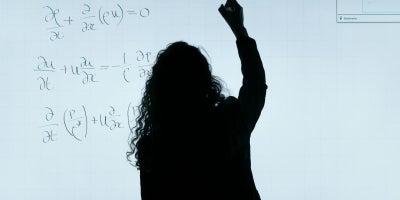 A female professor writing math equations on smart whiteboard in a classroom.
