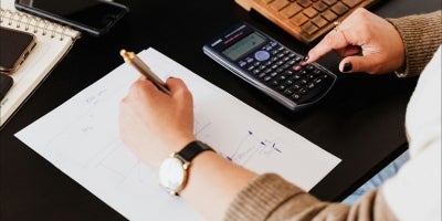 A female student sitting down with a desk solving math equations with a black calculator.