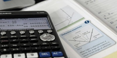 A close up of a calculator and a math textbook showing equations in a well-lit environment. 