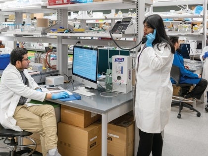 A BIO student in a lab coat answering a telephone and BIO student on the desktop in a lab facility.