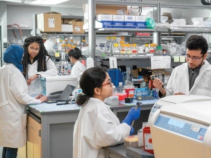 Multiple BIO students in lab coats conducting experiments in a laboratory facility.