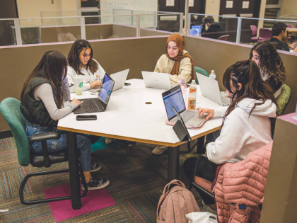 A group of five female students studying with laptops around a table at the CSU library.