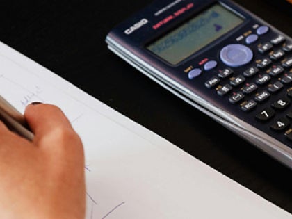 A female student sitting down with a desk solving math equations with a black calculator.