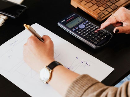 A female student sitting down with a desk solving math equations with a black calculator.