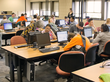 A well-lit classroom full of students working on math problems on computer desks.