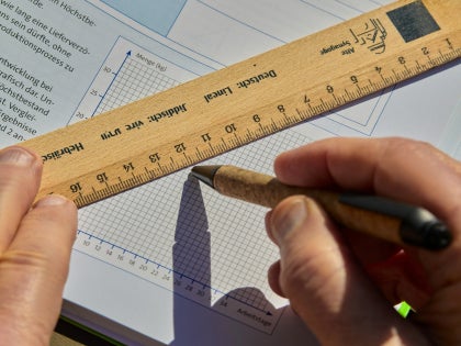 A student drawing a graph on a textbook with a ruler.