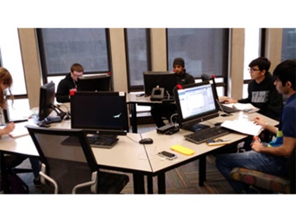 A group of students sitting and working on homework with computers in a classroom.