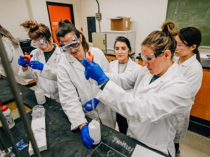 A group of students in white lab coats working on research in a lab.