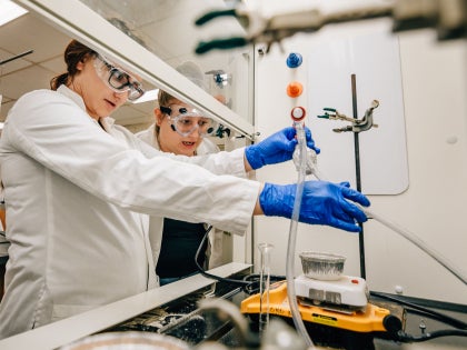 Two students in white lab coats handling research equipment in a lab.
